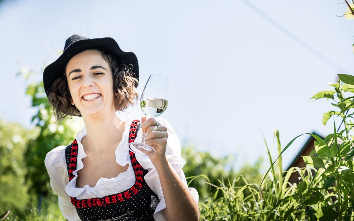 Frau sitzt waehrend dem Sommerurlaub in Bad Gleichenberg im Weingarten und haelt ein Glas Wein in der Hand