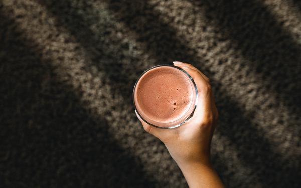 eine hand hält ein glas mit einem roten smoothie im vulkanlandhotel legenstein in die kamera